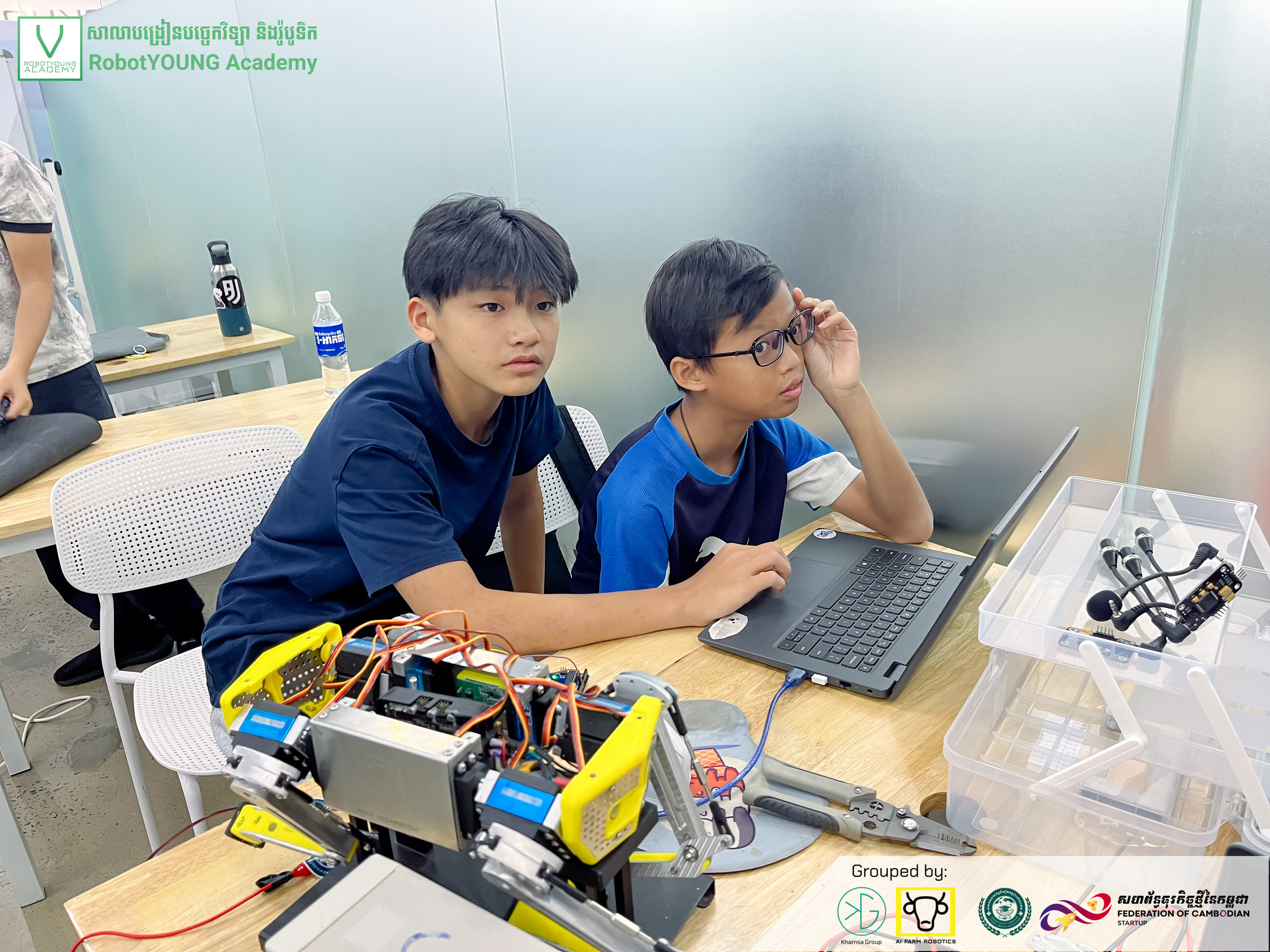 Two students working at a laptop beside a yellow quadruped robot and electronic components