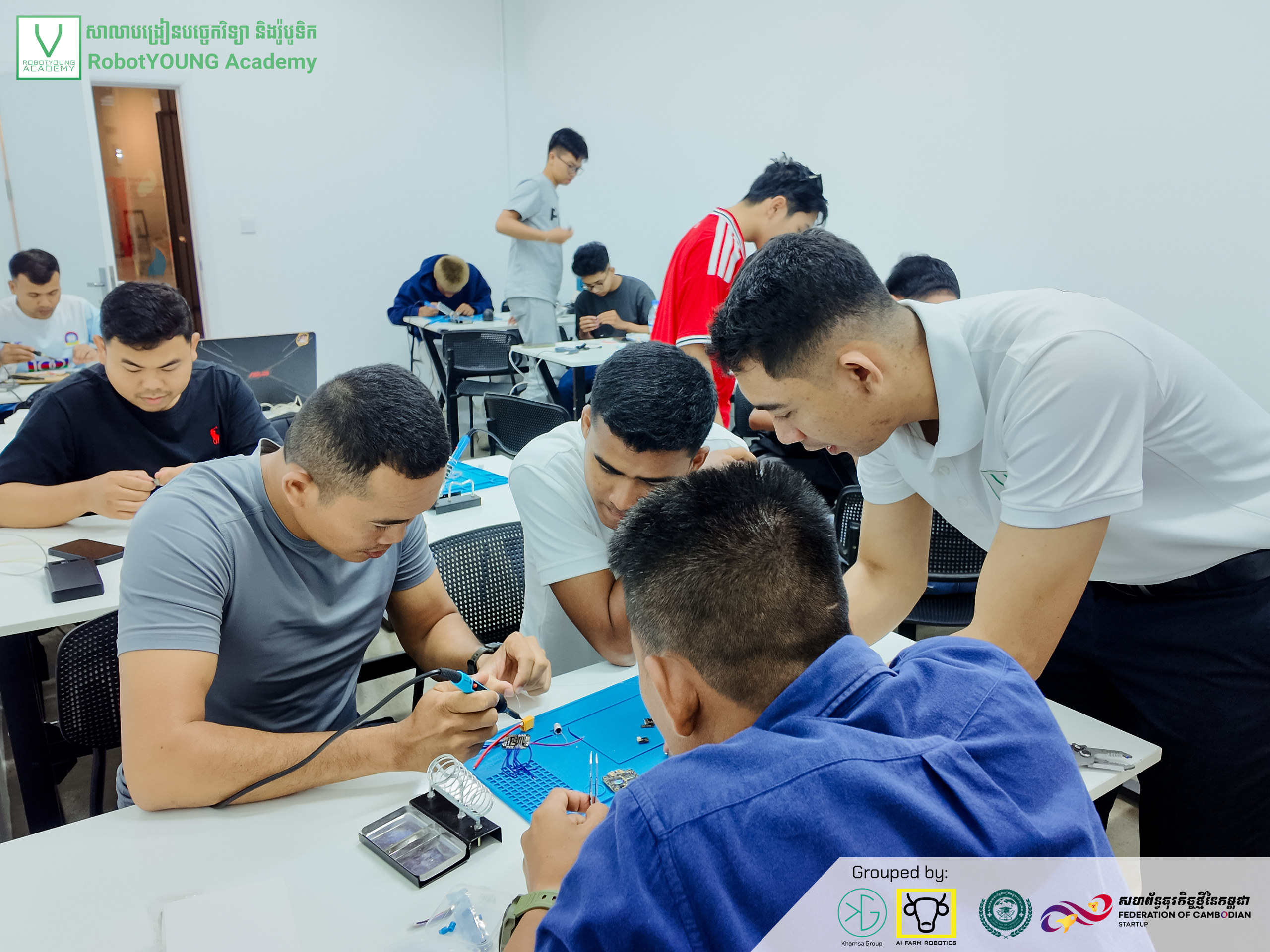 An instructor leaning over a table to guide learners assembling electronics on blue work mats