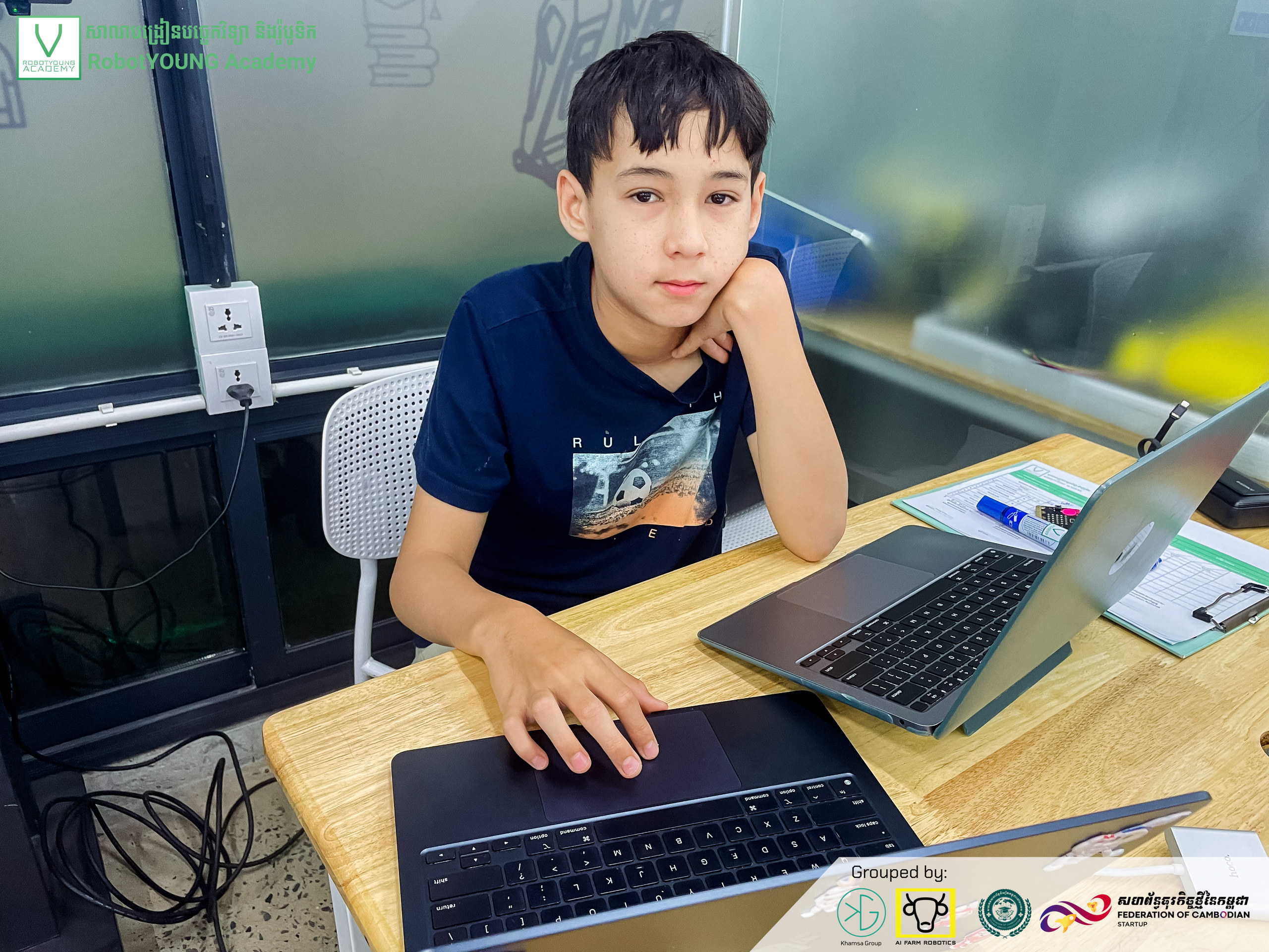 A student seated at a classroom table with two open laptops