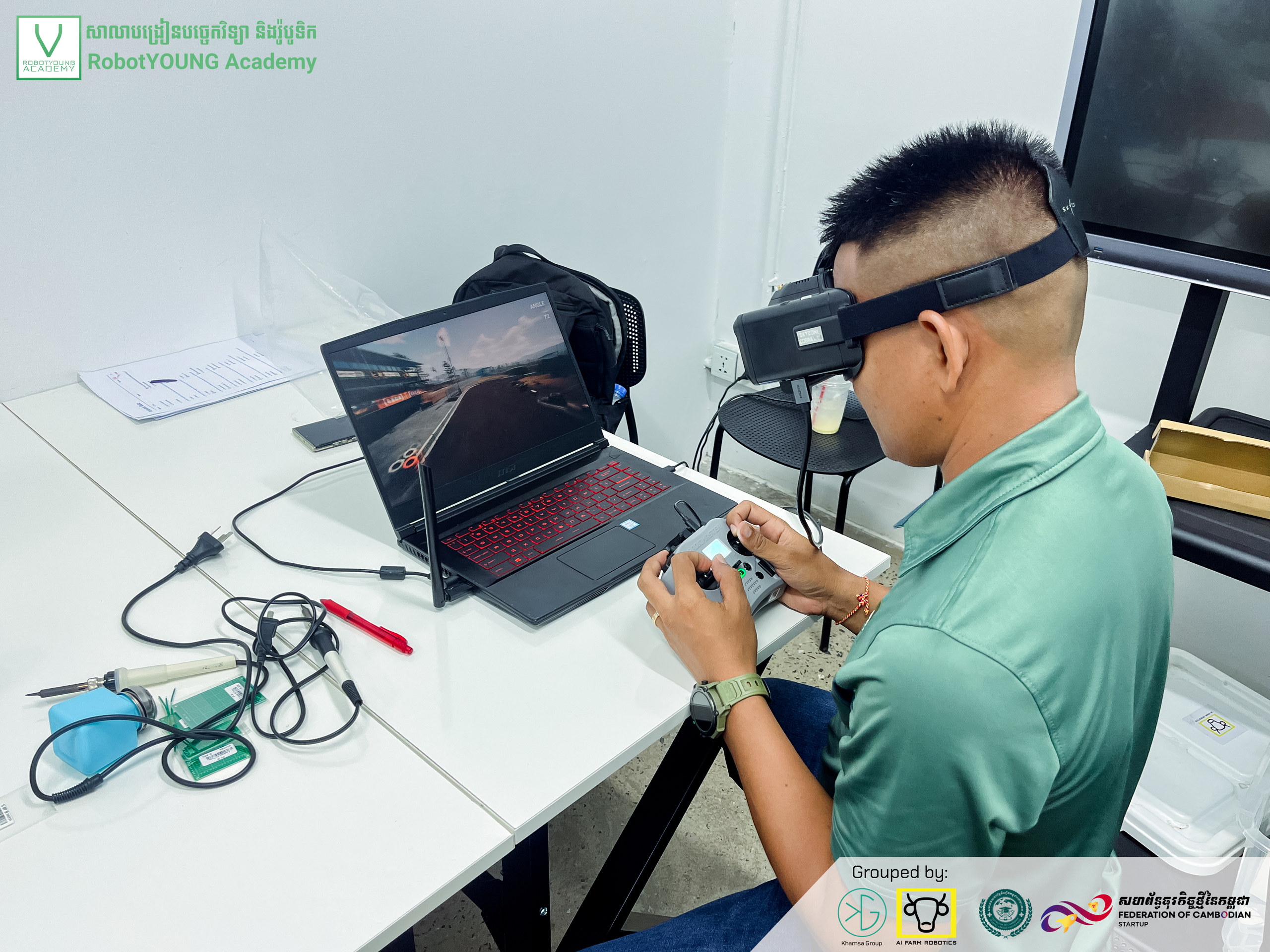 A learner wearing a magnifying headset working on electronics beside a laptop