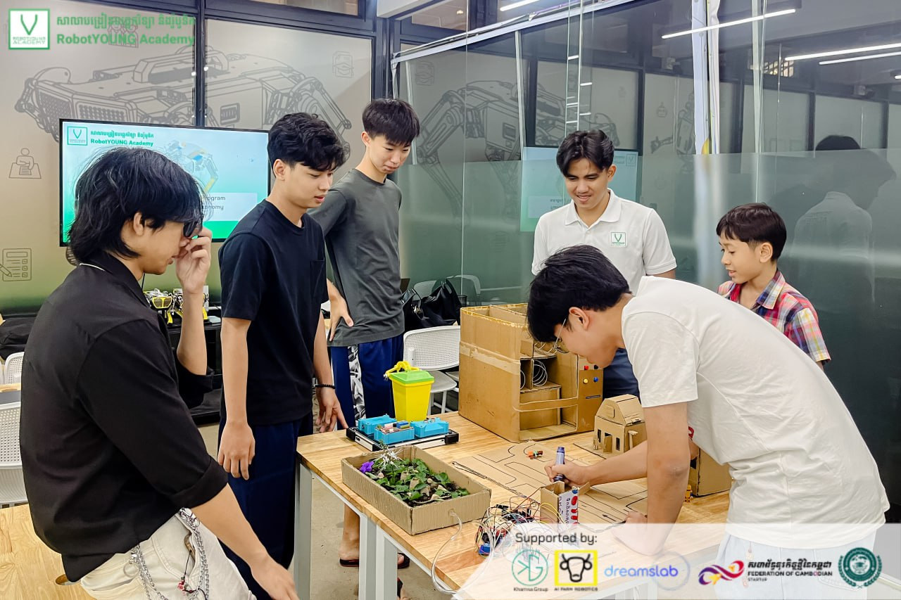 Students and an instructor demonstrating a cardboard model city with robots and electronics
